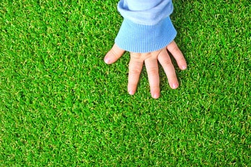 Child's hand touching artificial grass