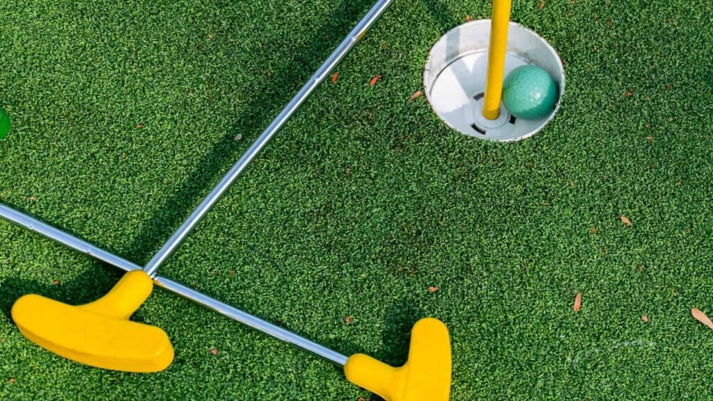 Putters on artificial turf putting green with golf ball in hole