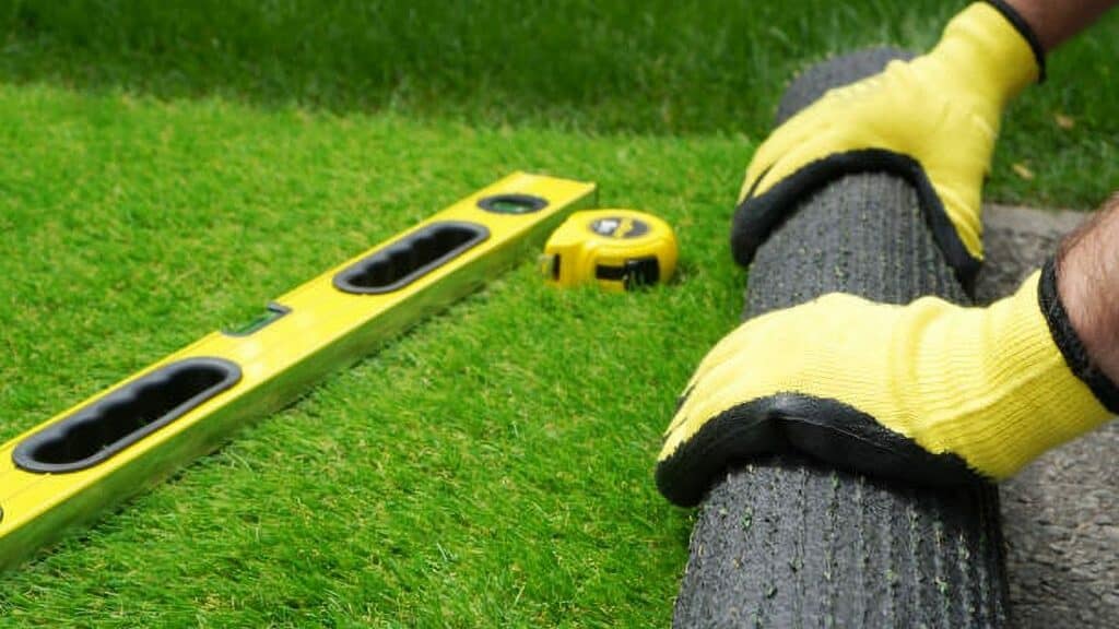 Professional with roll of artificial turf, yellow gloves, spirit level and tape measure