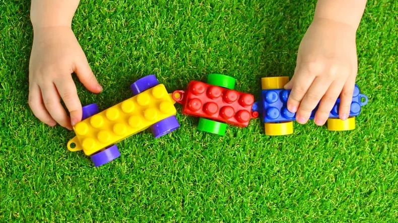 Child hands playing with lego train on artificial turf