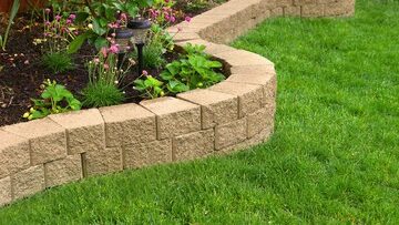 Landscaping with artificial turf around stone brick wall by flower bed