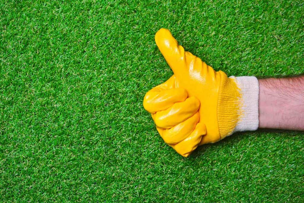Hand with yellow glove showing thumbs up on artificial grass background