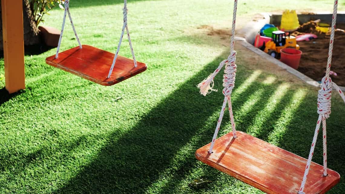 Kid's swing set and sandpit on artificial grass.